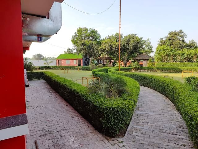 A paved path through the hedges at Manu Resort, with a gazebo beyond the lawn